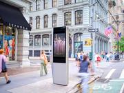 LinkNYC digital advertising kiosk on a busy New York City street corner, surrounded by pedestrians, cyclists, and storefronts.